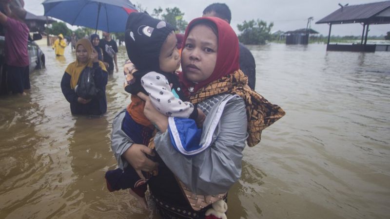 Warga menggendong anaknya melintasi banjir di Desa Kampung Melayu, Kabupaten Banjar, Kalimantan Selatan, Jumat (15/01). Banjir ini digambarkan sebagai banjir terbesar yang melanda provinsi tersebut.(foto:BBCIndonesia)