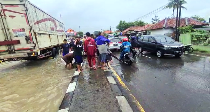 Warga bergotong-royong terpaksa membongkar median jalan guna mempercepat aliran air yang menggenangi rumah-rumah warga. (Taryani)
