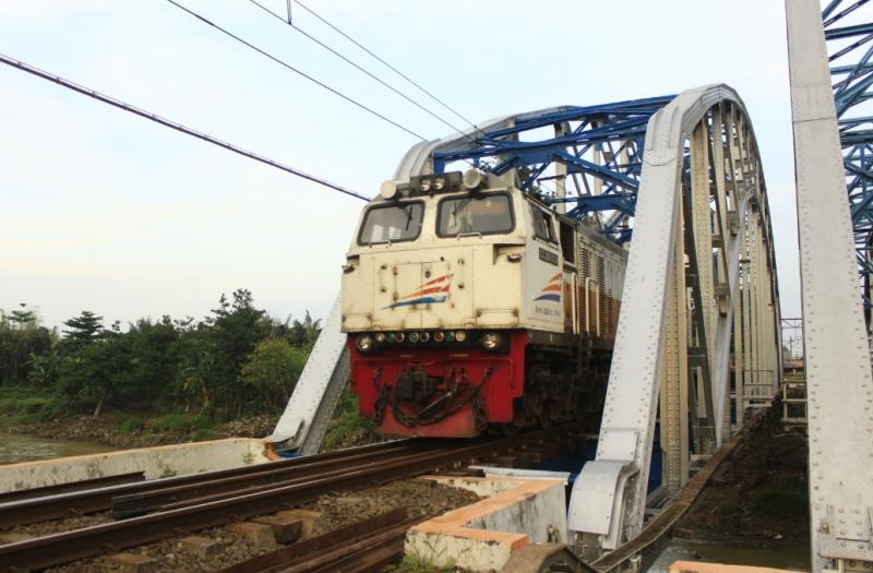 Kereta api melaju di jembatan sungai di Bekasi.