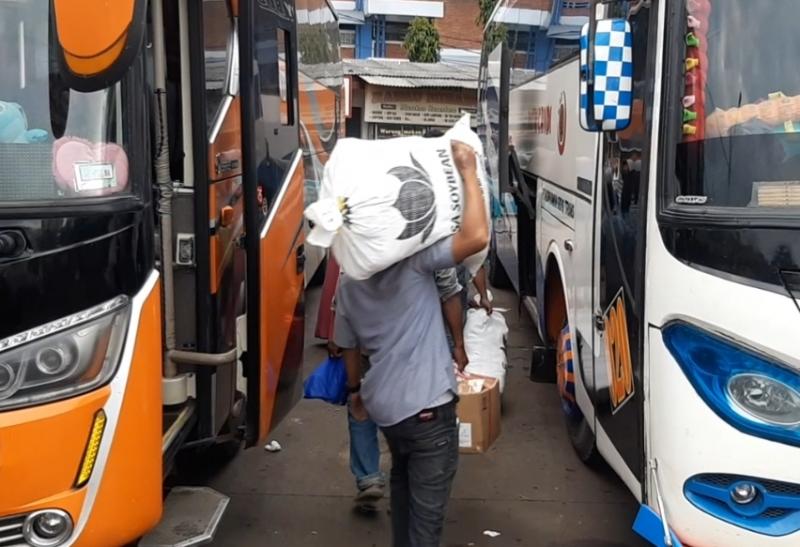 Kru bus tengah memikul barang bawaan penumpang untuk dimasukkan ke bagasi bus Putri Candi.