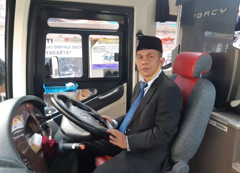 Pengemudi bus Harapan Jaya, Nahrowi tengah mengendari busnya bergaya bak pejabat menggunakan jas lengkap dengan dasi dan peci.