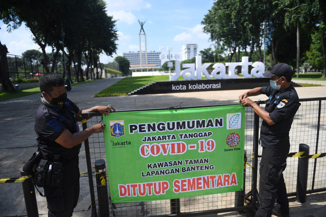 Petugas gabungan merapikan spanduk pengumuman ditutupnya Taman Lapangan Banteng di Jakarta, Jumat (25/6/2021). Foto: Akbar Nugroho Gumay/Antara Foto