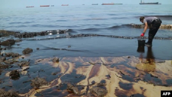 Foto ini diambil pada 2 April 2018 menunjukkan seorang polisi berusaha membersihkan Pantai Benua Patra setelah terjadi tumpahan minyak di dekatnya di Balikpapan. (Foto: AFP)