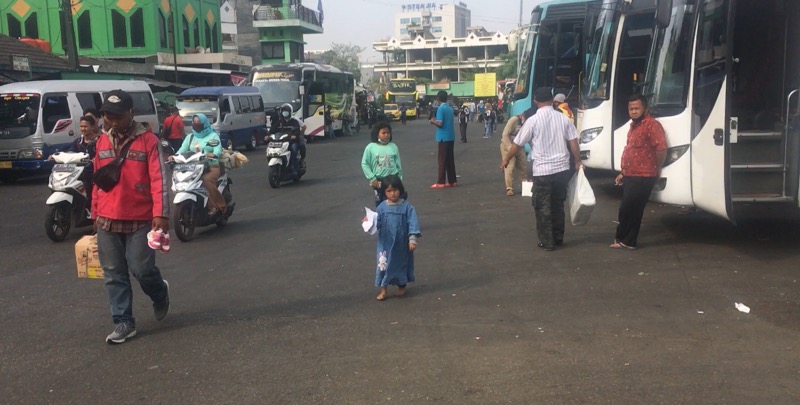Dua orang bocah/anak kecil tengah berjalan bersama orang tuanya tepat di depan deretan bus antarkota, Kamis (19/8/2021). Foto: BeritaTrans.com.