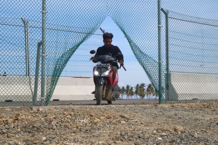 Salah seorang warga terlihat melintasi pagar sirkuit MotoGP yang dirusak, Jumat (20/8/2021). Foto: Kompas.com.