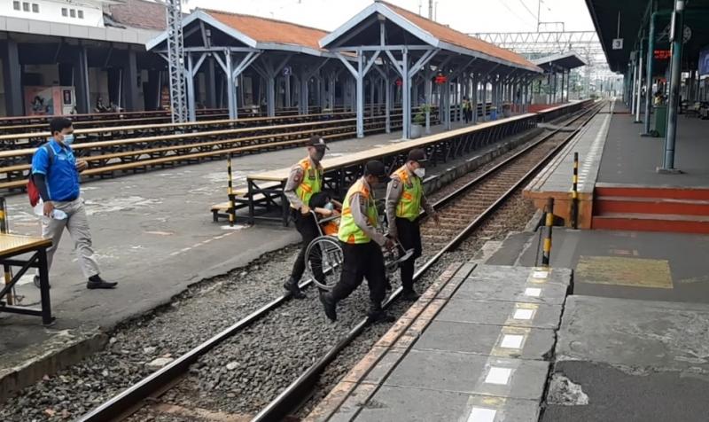 Satpam mengangkat seorang penumpang KRL untuk menyeberangi rel menuju peron keberangkatannya di Stasiun Manggarai, Selasa (5/10/2021).