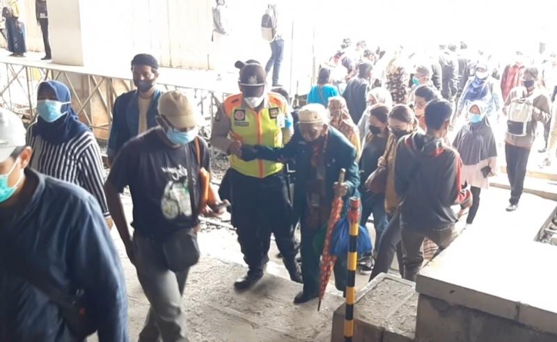 Seorang petugas membantu penumpang KRL menyeberangi perlintasan di Stasiun Manggarai.