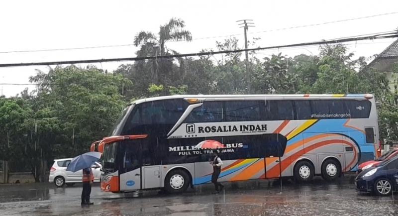 Dengan menggunkan payung saathujan, pramugari bus dengan juru parkir bersama mengarahkan bus agar aman untuk mundur saat bus hendak keluar pool bus Rosalia Indah di Bulak Kapal, Bekasi, Kamis (20/1/2022)