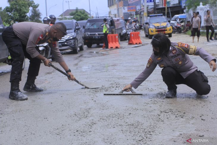 Dua orang aparat kepolisian sedang menambal titik jalan berlubang di Kupang Kota cegah laka lantas. (Foto:Antara)