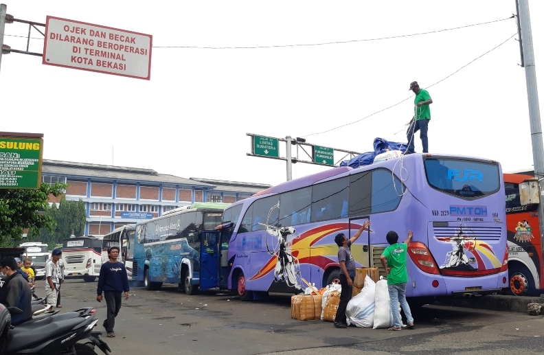 Bus PMTOH menaikan barang bawaan penumpang ke atas busnya saat mengetem di Terminal Bekasi, Ahad (30/1/2022)