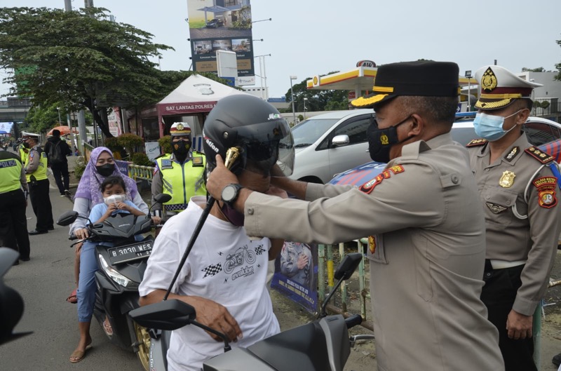 Kapolres Metro Bekasi Kota, Kombes Pol Hengki measangkan helm kepada pengendara sepeda motor yang kedapatan tidak menggunakan helm, Kamis (10/3/2022). Foto: istimewa.