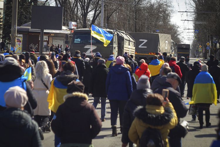 Orang-orang membawa bendera Ukraina berjalan menuju truk tentara Rusia saat unjuk rasa menentang pendudukan Rusia di Kherson, Ukraina, Minggu (20/3/2022). PBB mengecam intimidasi yang dilakukan Rusia terhadap warga yang menentang perang Rusia.(AP PHOTO/OLEXANDR CHORNYI)