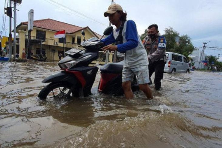 Petugas kepolisian membantu warga Jakarta Utara mendorong sepeda motornya yang mogok akibat terendam banjir rob. 